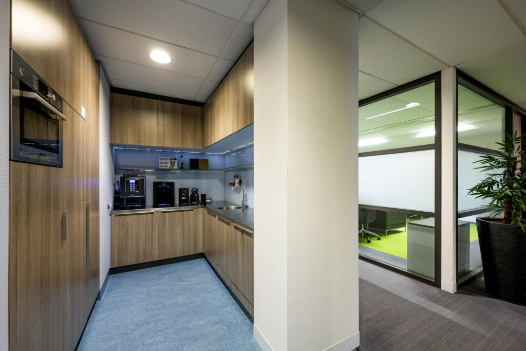 Kleine, moderne pantry met koffiezetapparaten en houten kasten in een kantoorpand aan de Laan van de Helende Meesters.